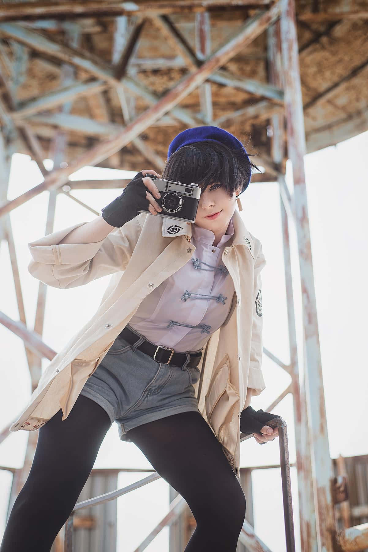 持相機的Cosplay角色 壁紙 — 一名穿著角色扮演服裝的人士在生鏽的金屬結構內自信地擺姿勢，手持一部復古相機。