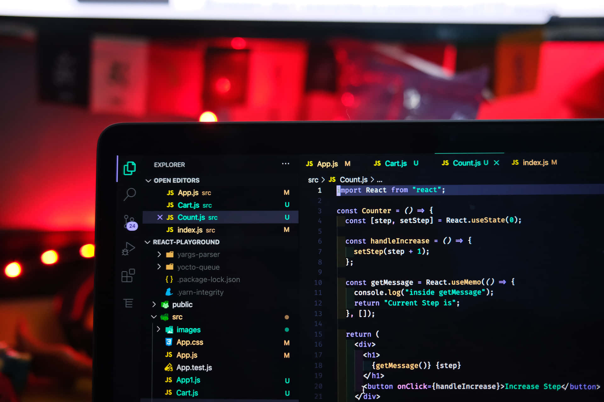 手提電腦屏幕在科技工作空間中顯示帶有紅色環境照明的 React 代碼。