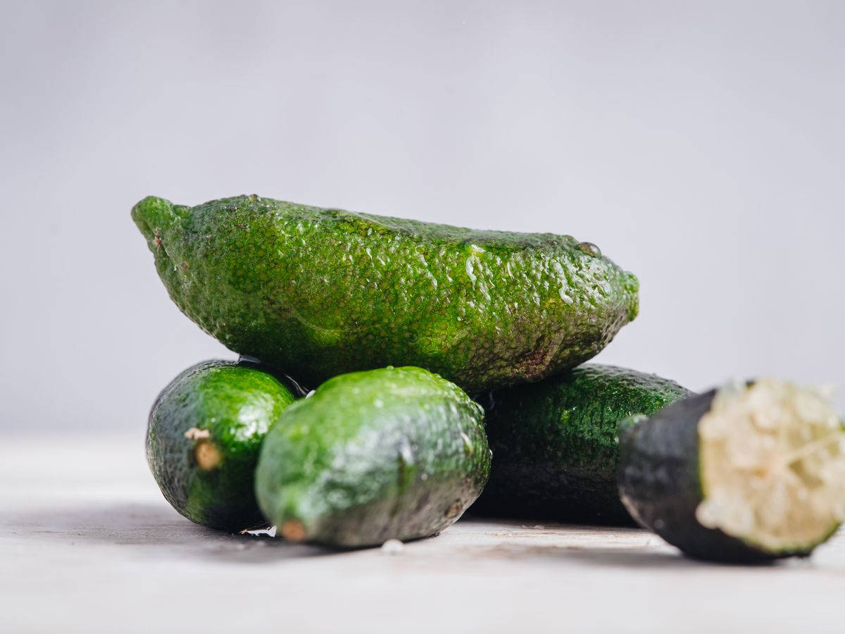 指 lime 照片 壁紙 — 一堆新鮮青檸，其中一個切開露出淡色果肉，襯以柔和灰色背景。