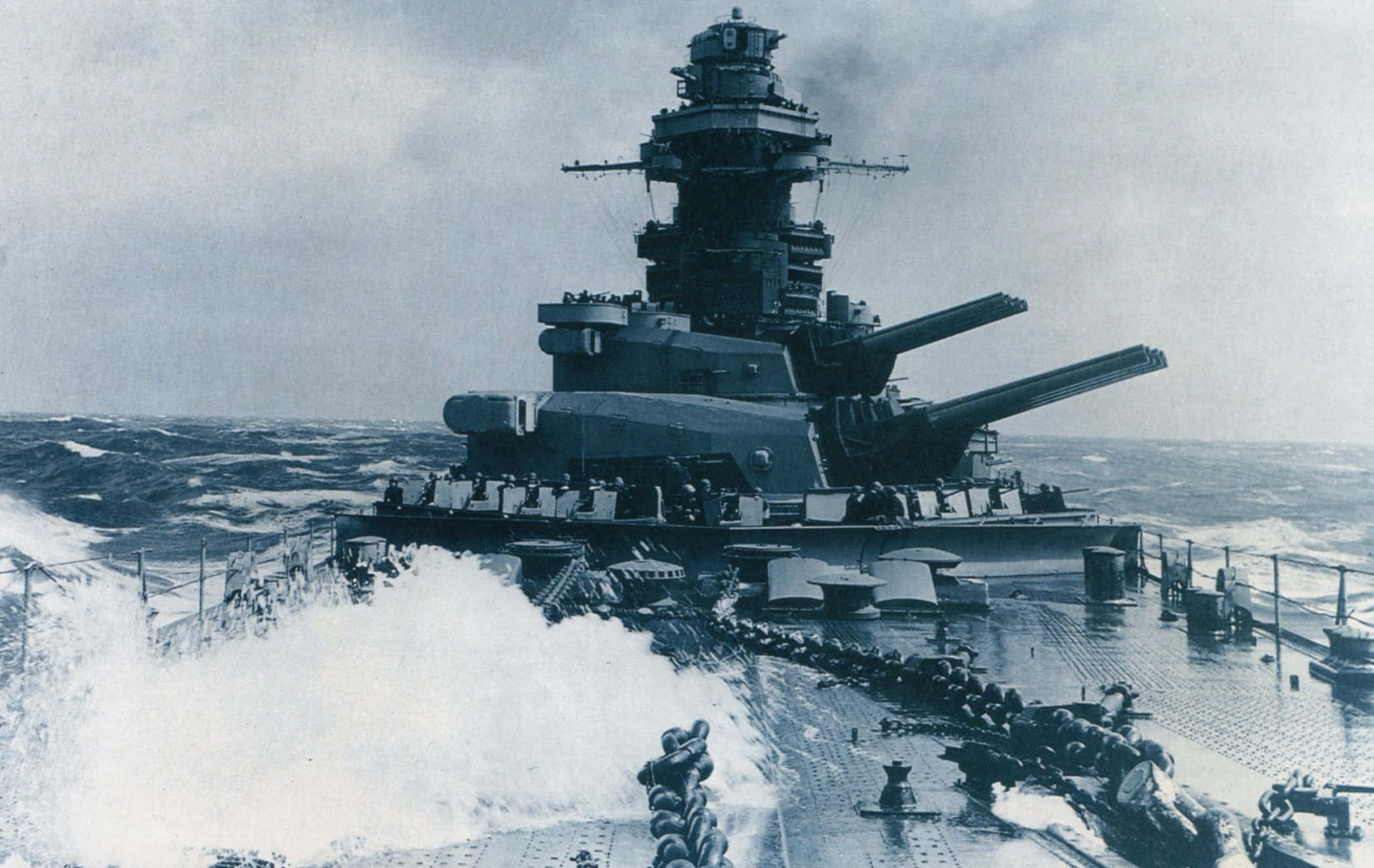 指揮現代戰艦 壁紙 — 一艘巨大的戰艦在陰天中破浪前行，海浪拍打甲板。