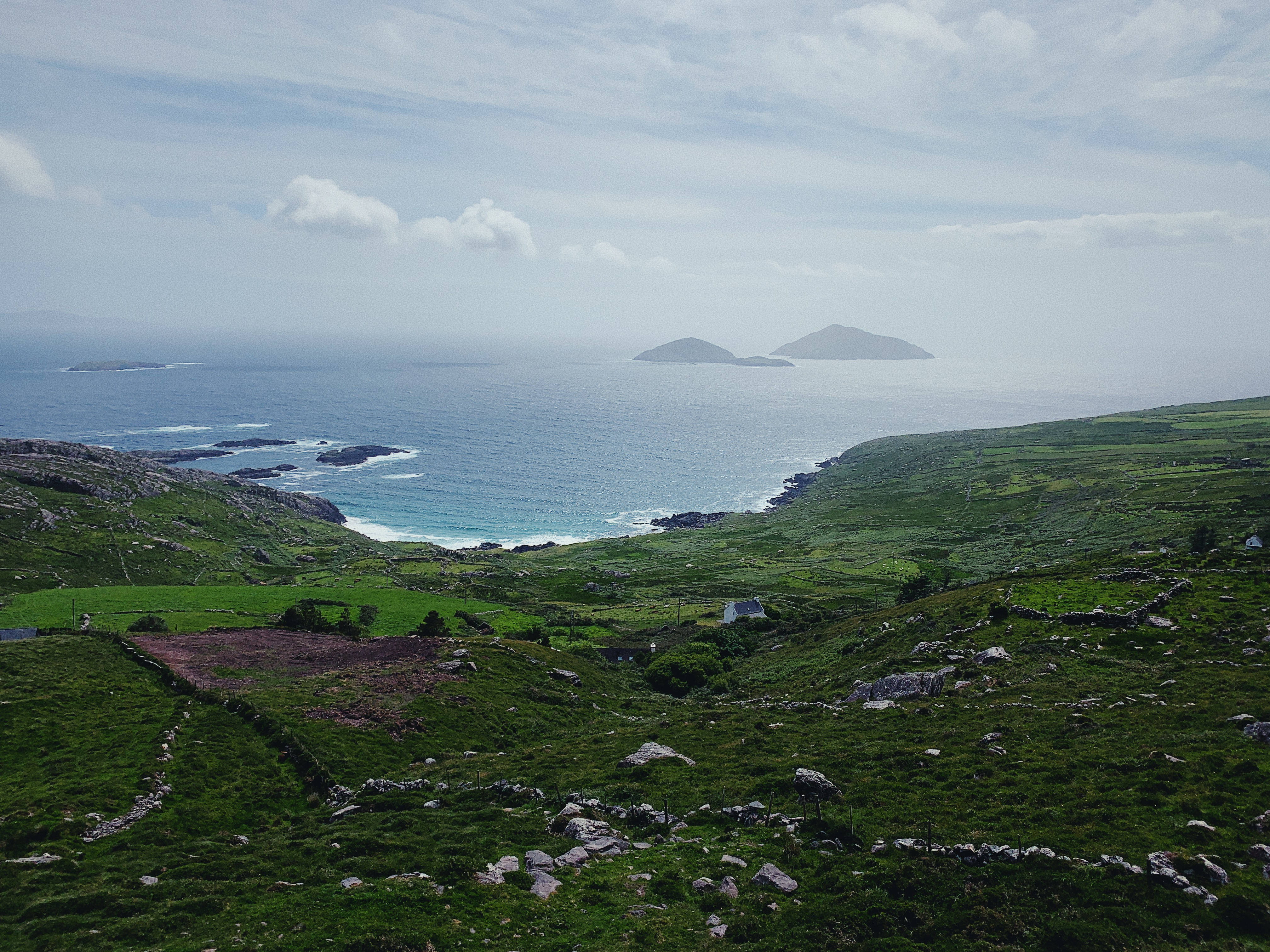 《指環王：力量之戒》努門諾爾的壯麗風景 壁紙 — 霧氣瀰漫的海岸景觀，起伏的綠色山丘點綴著石牆，地平線上有遙遠的島嶼。