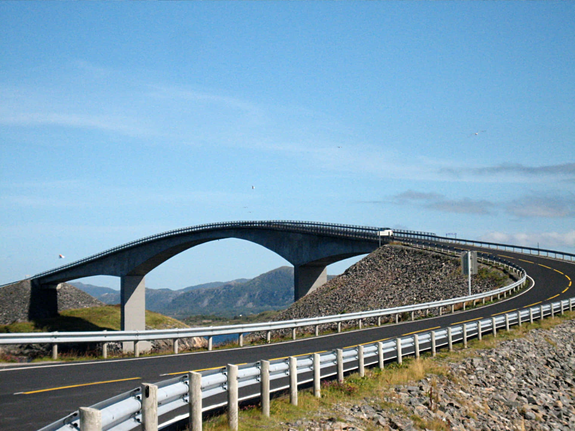彎曲的高速公路橋樑橫跨岩石地形，背景有山脈。