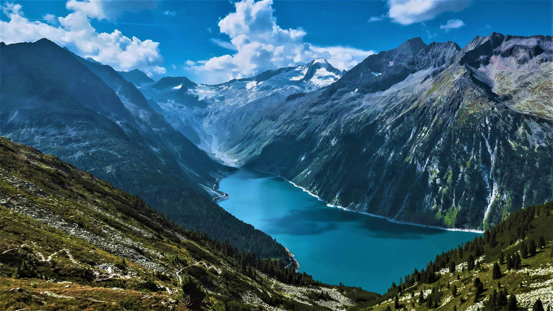 一個碧綠的湖泊，周圍是崎嶇的山脈，山頂積雪，山坡翠綠。