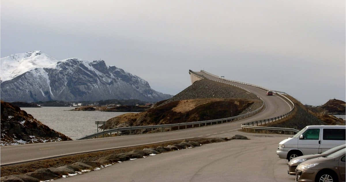 蜿蜒的海岸道路，雪山和停放的汽車在灰色天空下。