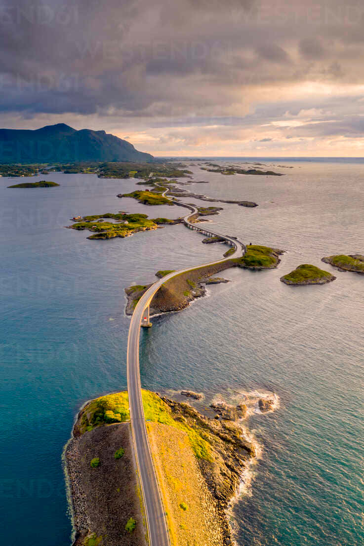 一條蜿蜒的海岸公路在日落時分以戲劇性的雲彩連接島嶼。