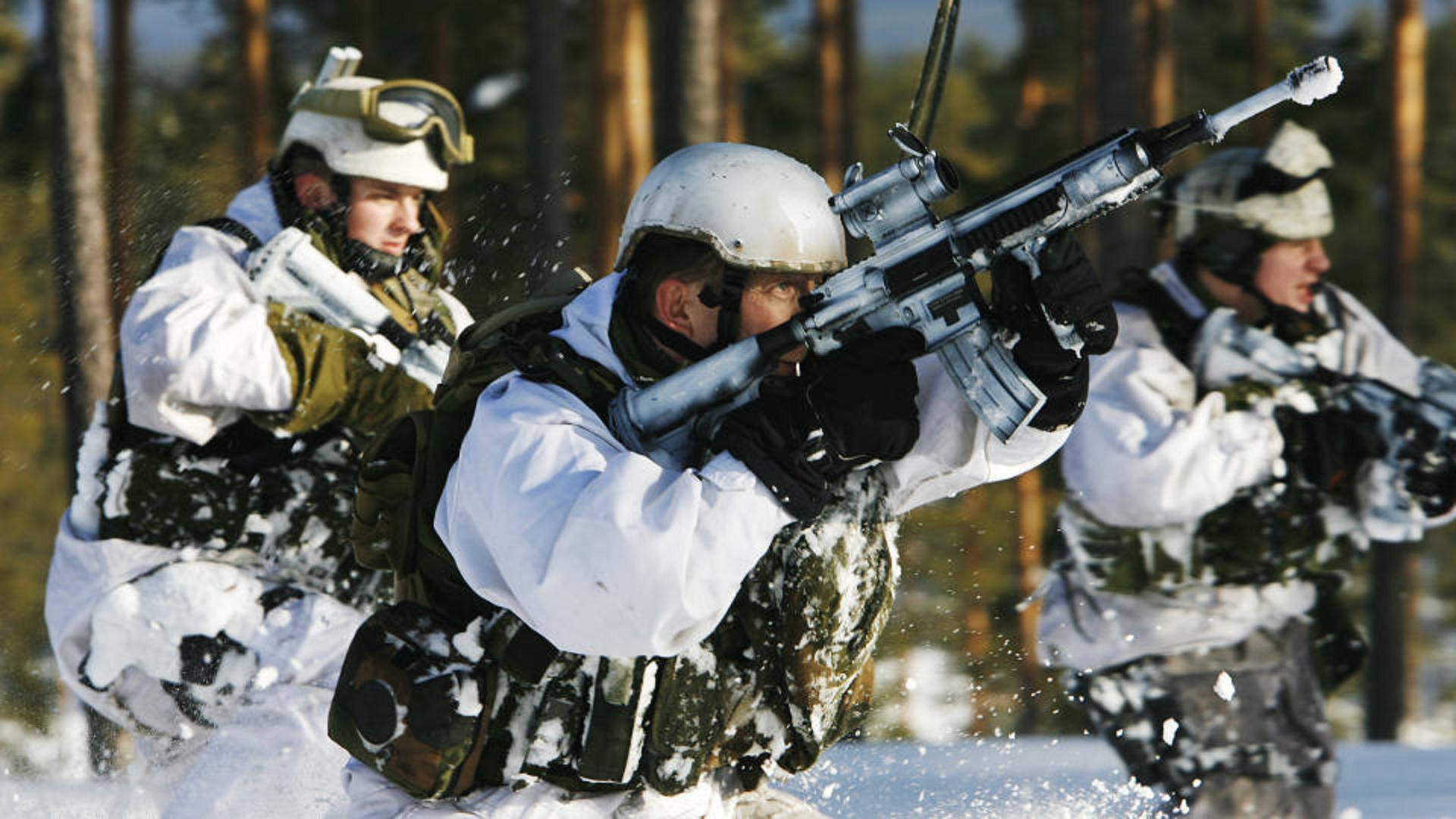 穿著冬季迷彩服的士兵在積雪覆蓋的森林中持步槍前進。