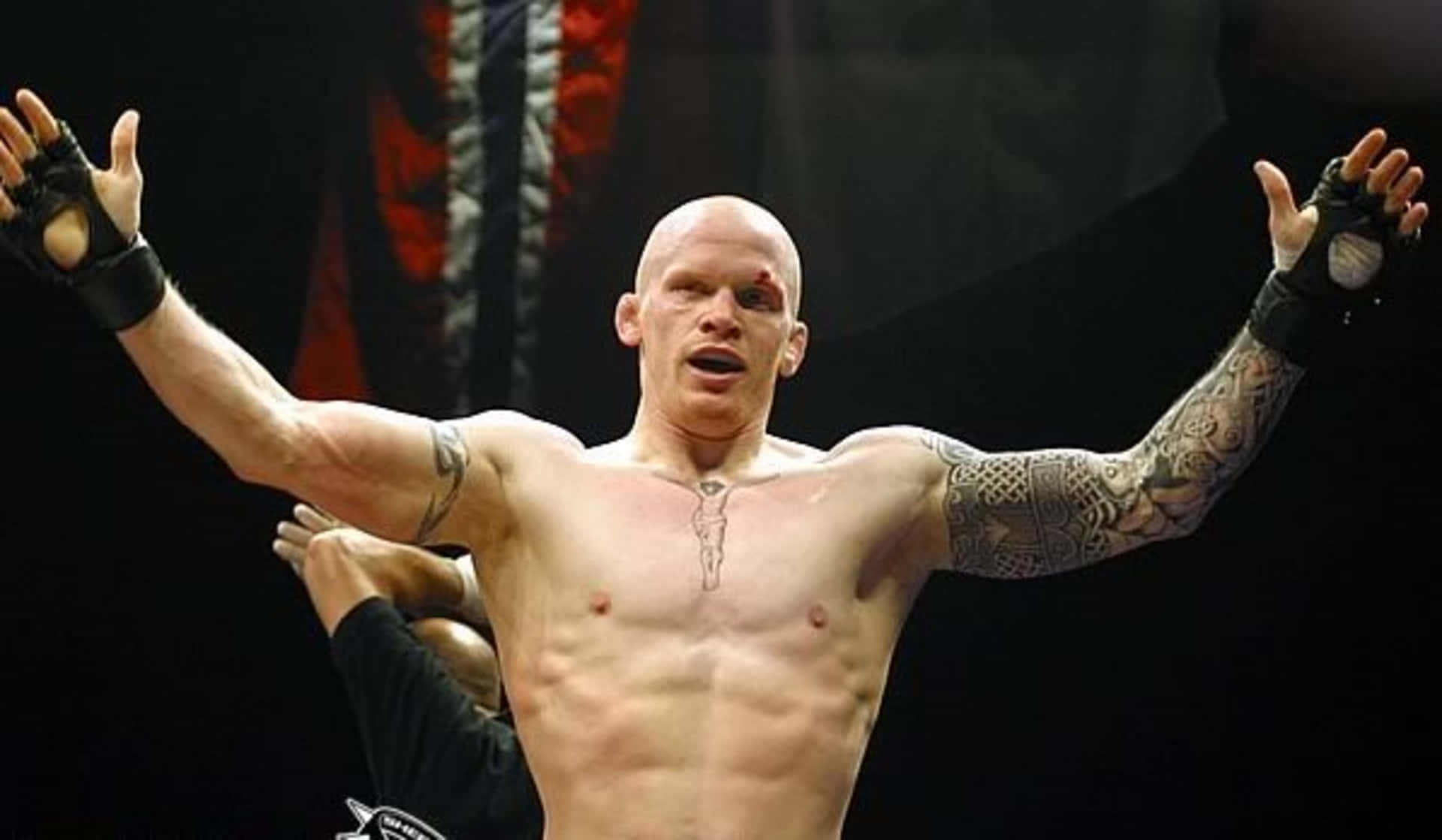 挪威職業MMA選手約阿希姆·漢森專注比賽 壁紙 — 一位光頭肌肉發達的戰士，身上有紋身，在昏暗的競技場中高舉雙臂慶祝勝利。