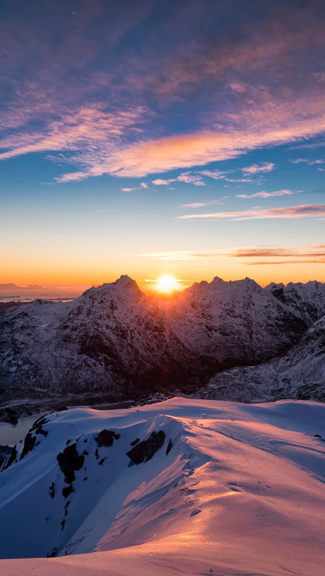 積雪的山峰沐浴在金色的夕陽光中，上方有色彩繽紛的雲彩。