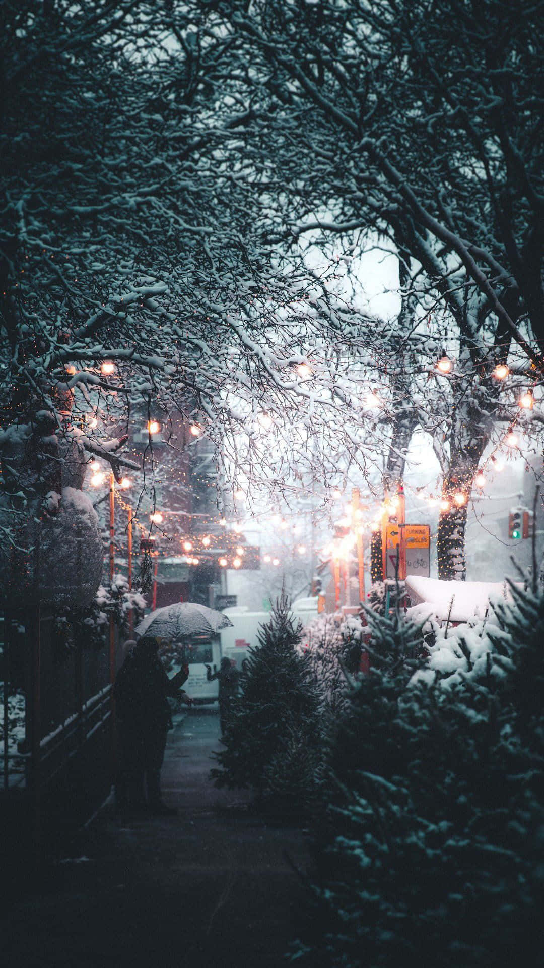 夜晚在燈串下撐傘在雪中行走的人