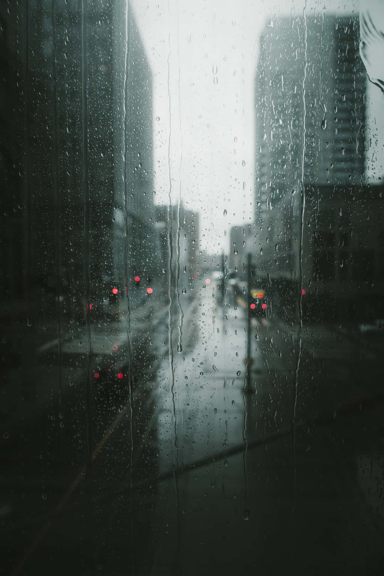 雨滴沿著窗戶流下，顯示出一條昏暗的城市街道，暮色中有紅色車燈。