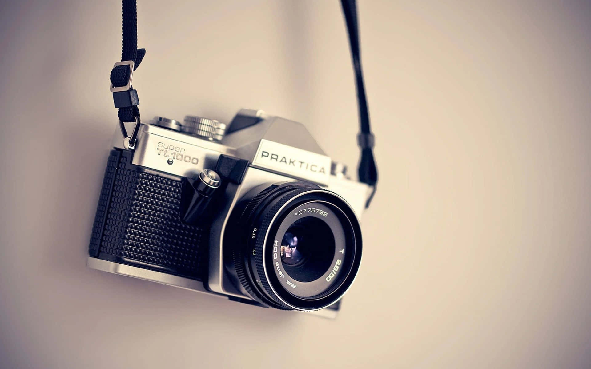 復古Praktica TL1000菲林相機用掛帶掛在米色牆上。