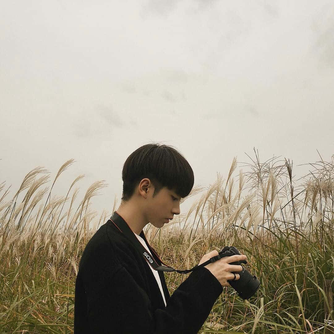 年輕男子在多雲天氣中站在高草叢中手持相機