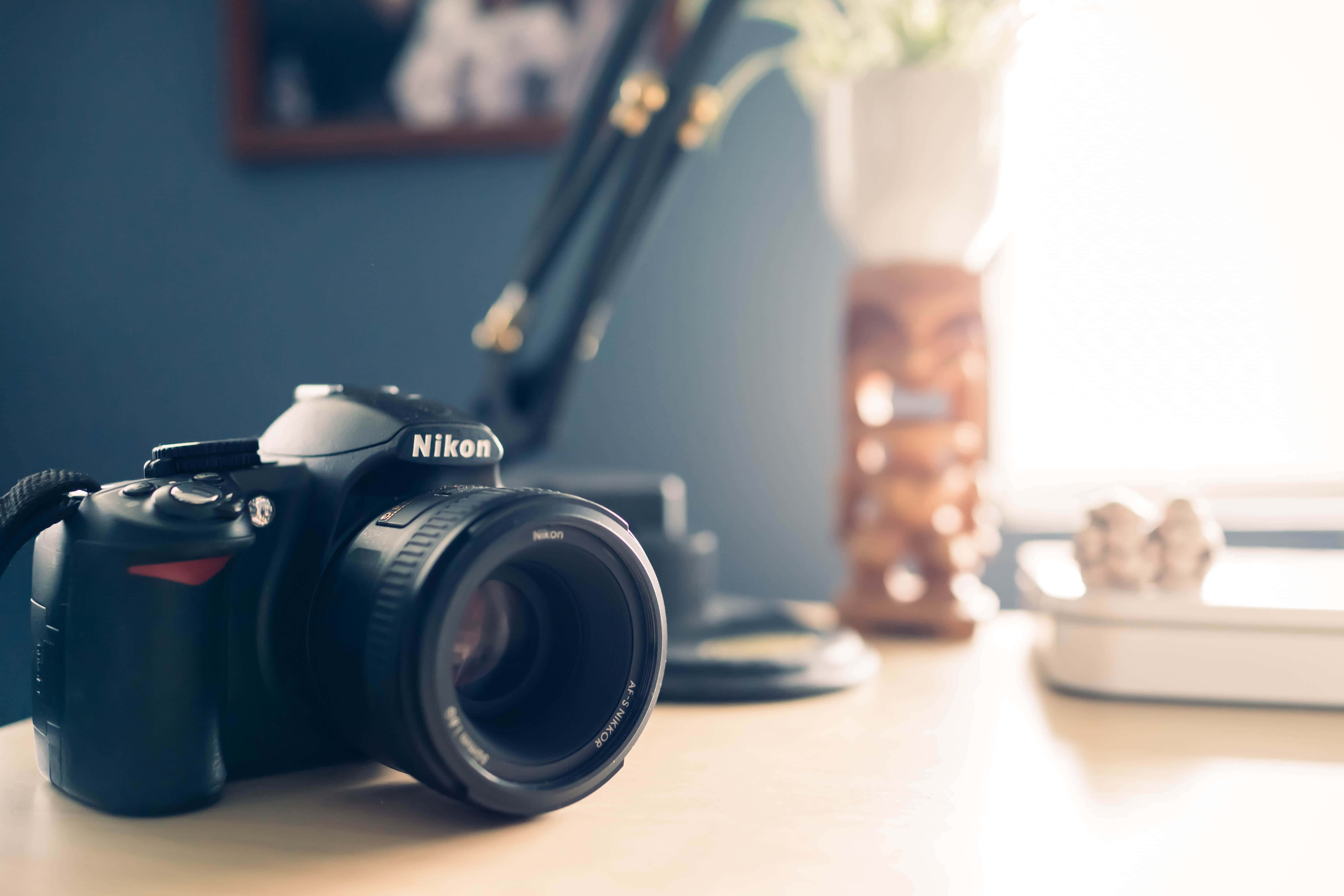 捕捉瞬間：單眼攝影 壁紙 — 一部黑色Nikon DSLR相機放在木桌上，柔和自然光從裝飾花瓶後的窗戶射入。