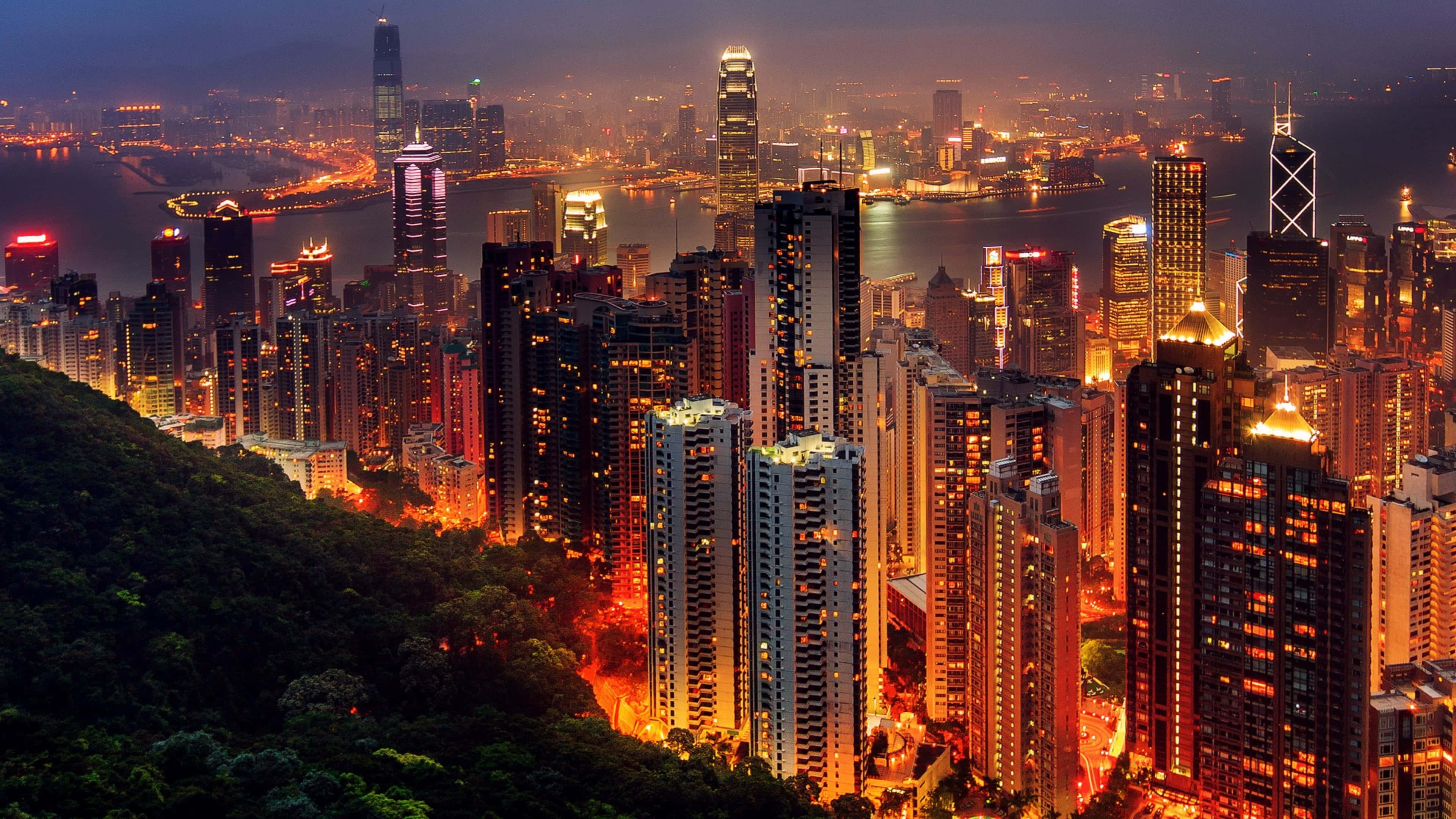 捕捉自然之美 壁紙 — 香港在黃昏時分的空中景觀，密集的摩天大樓和港口反射著溫暖的城市燈光，天際線閃爍發光。