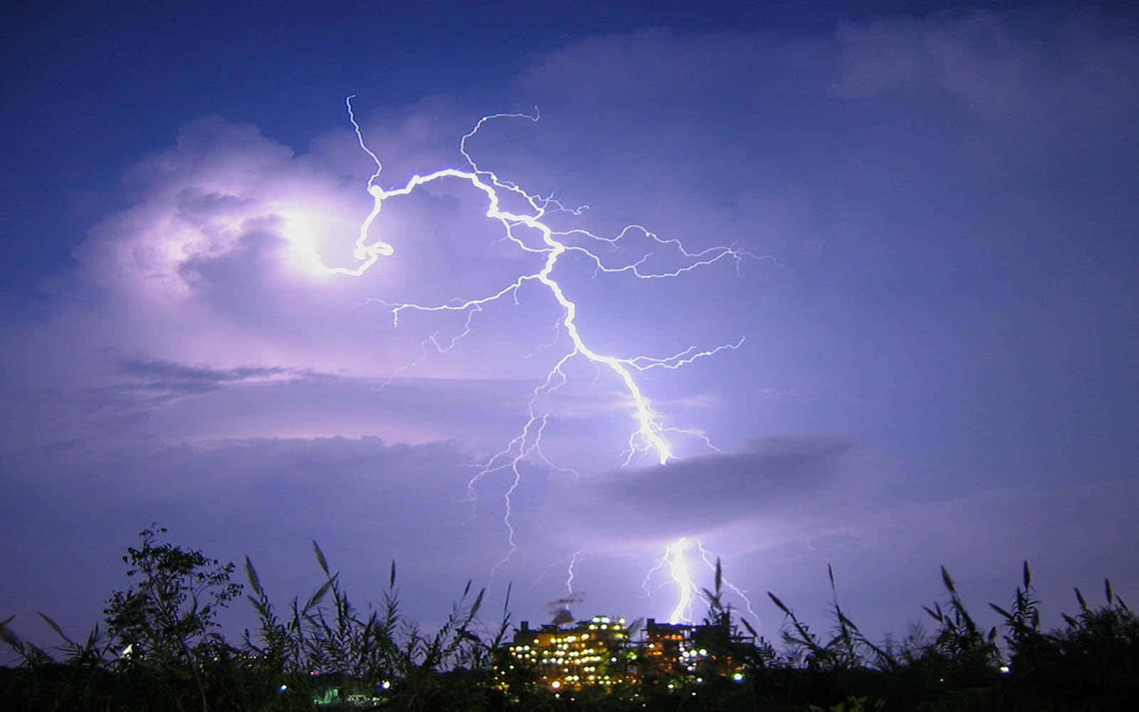 閃電在夜間城市上空閃爍，伴隨著紫色雲朵和剪影般的草地。