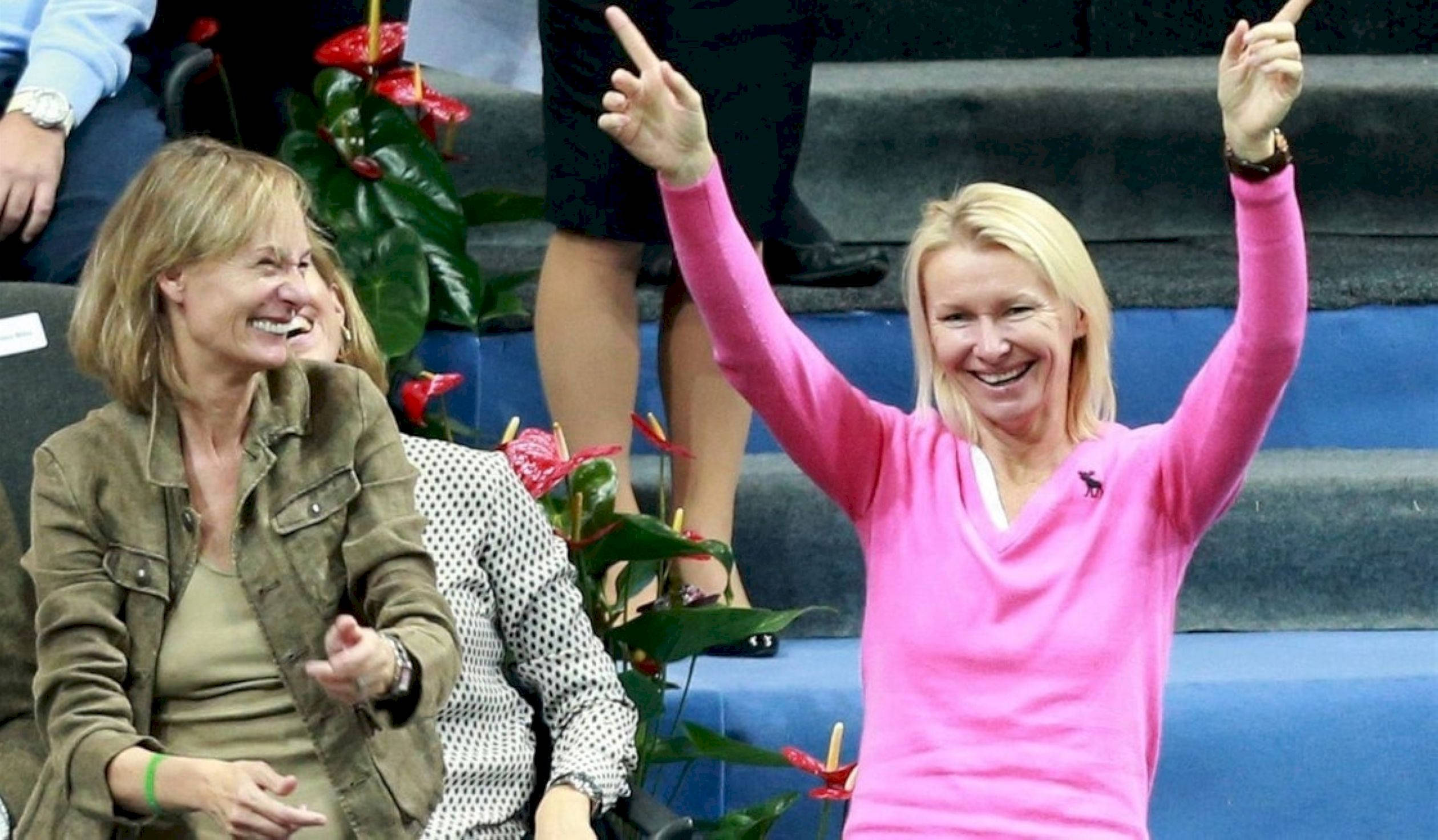 捷克網球名將 Jana Novotna 與波蘭選手 Iwona Kuczyńska 壁紙 — 兩名女子在體育場開心地慶祝，其中一人穿著亮粉紅色毛衣，興奮地高舉雙手。