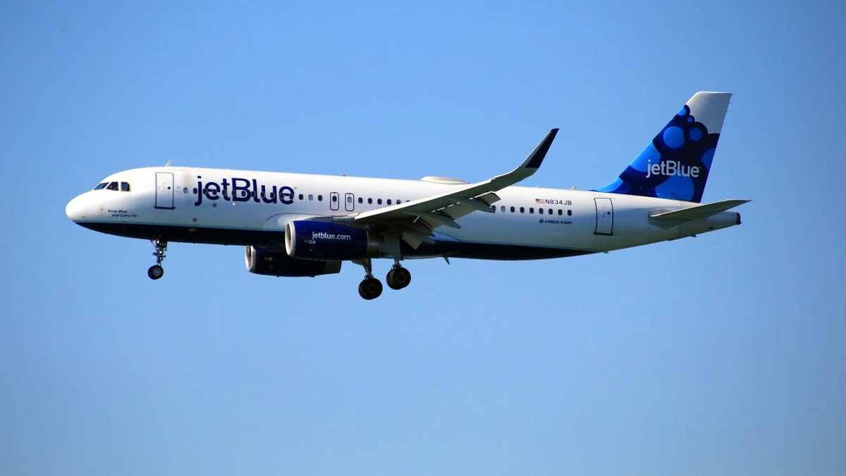 JetBlue 飛機在晴朗藍天下飛行，起落架已伸出。