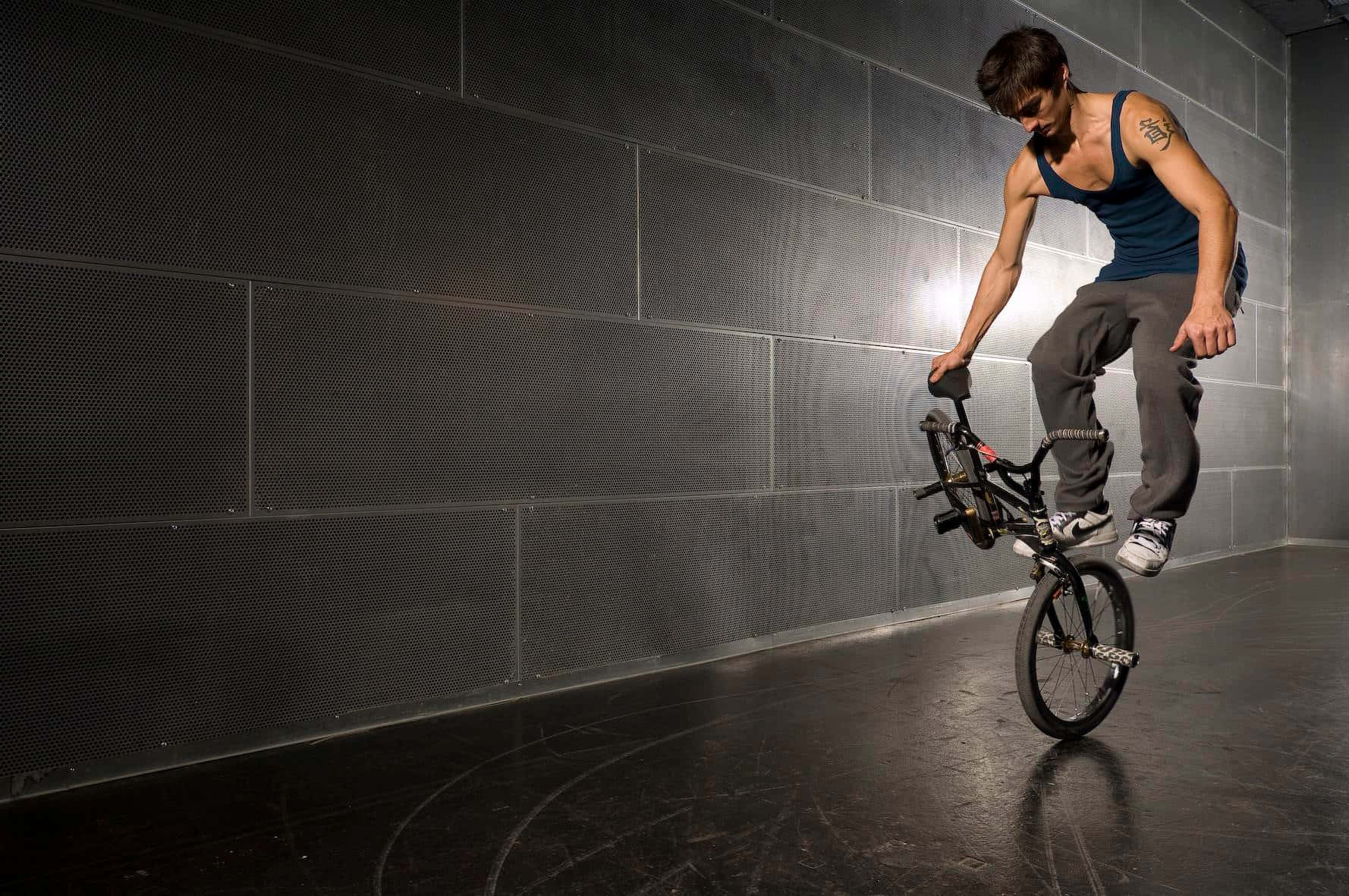 BMX車手在室內對著深色穿孔牆壁翹孤輪。