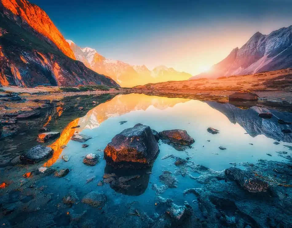 夕陽映照在岩石環繞的寧靜高山湖泊中的山巒。