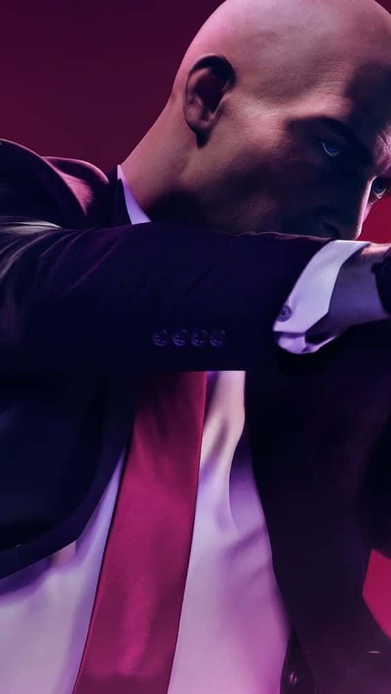 探索《Hitman 2》的世界 壁紙 — 一個光頭男子身穿深色西裝和紅色領帶，在戲劇性的紫色燈光下，以銳利的藍色眼睛向前傾。