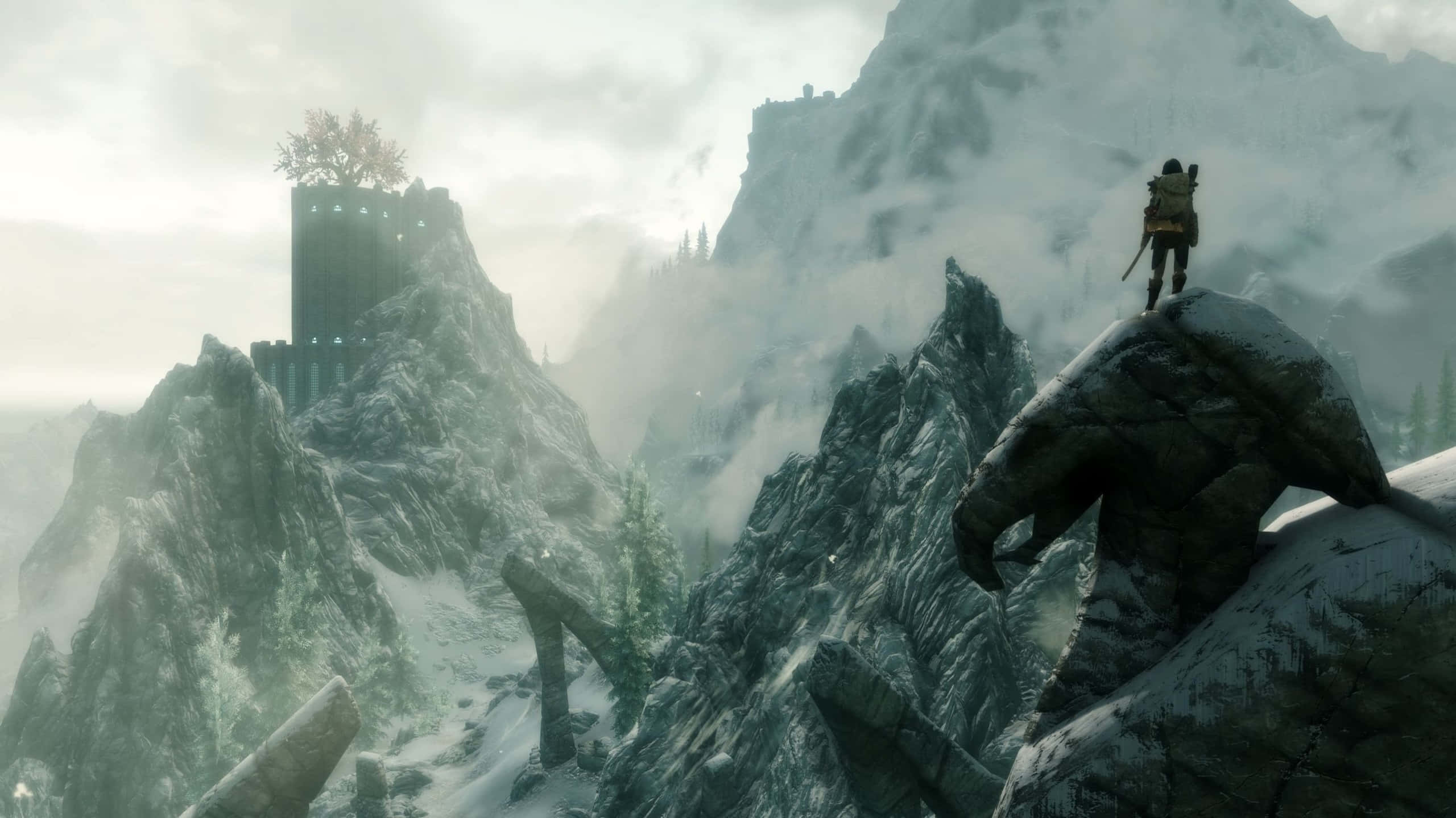 探索《Skyrim》的世界 壁紙 — 一個孤獨的戰士站在白雪覆蓋的山頂上，俯瞰著霧氣瀰漫的山谷，山谷中有古老的廢墟和遠處塔樓上的一棵孤樹。