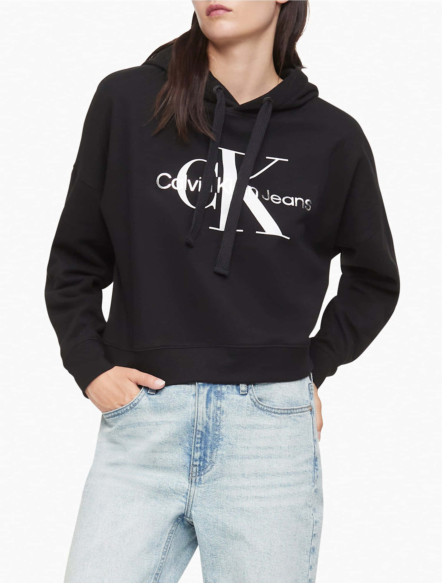 探索Calvin Klein的多元表達 壁紙 — 一個人穿著黑色短版連帽衛衣，帶有白色Calvin Klein標誌，配淺藍色牛仔褲，背景為純白色。