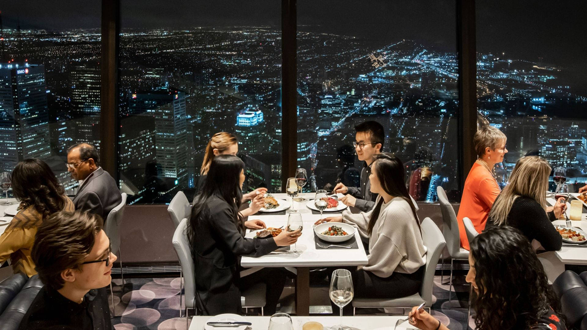 一群人在屋頂餐廳用餐，俯瞰夜晚充滿活力的城市。