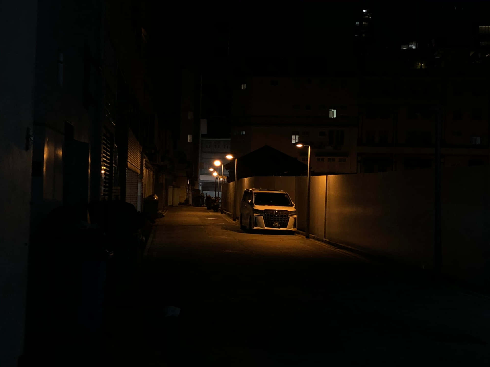 夜間白色貨車停泊在黑暗小巷中，被路燈照亮。