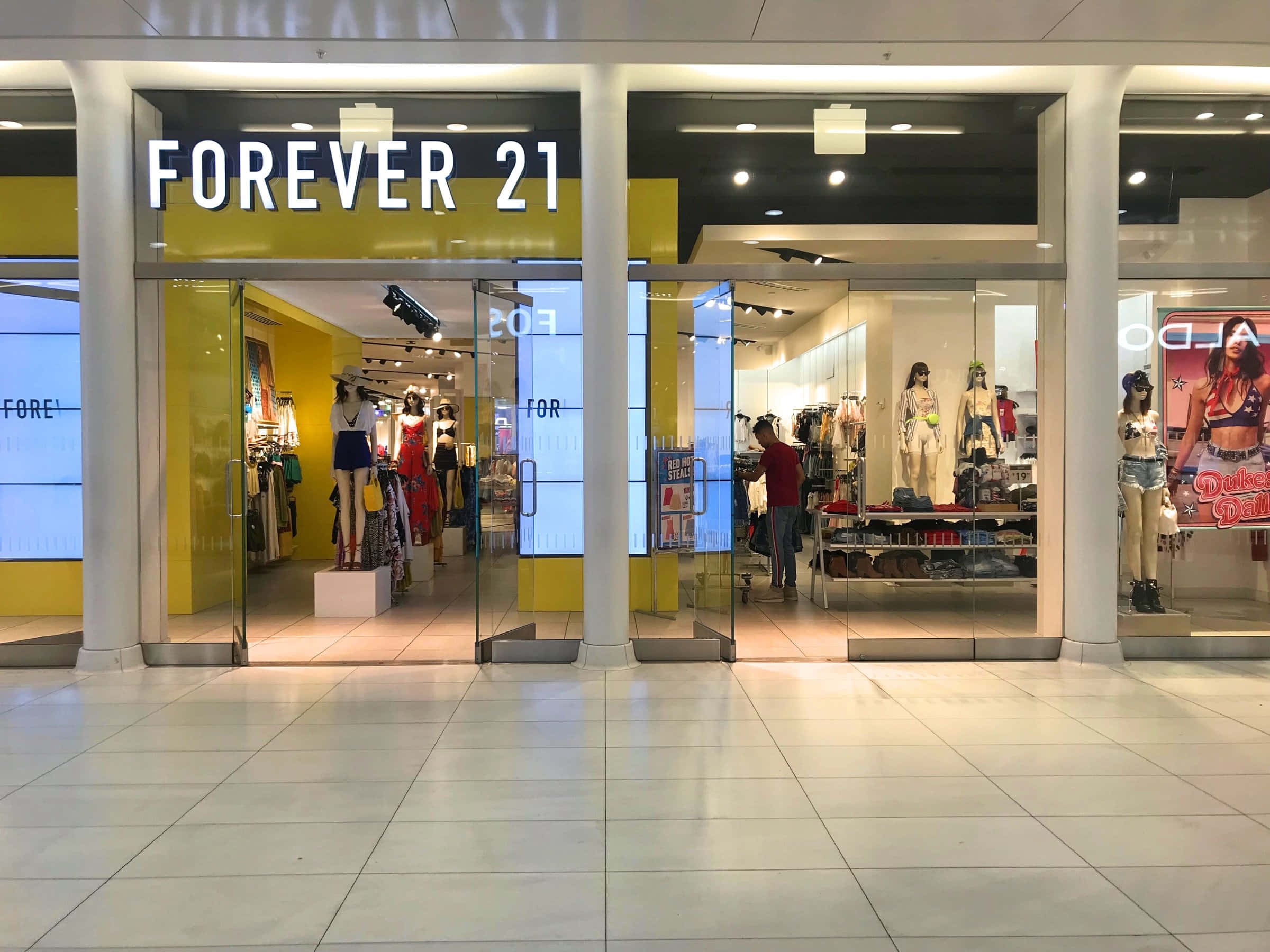 探索Forever 21最新潮流，打造個人風格 壁紙 — 購物中心內一間Forever 21商店燈光明亮的入口，人體模型展示色彩繽紛的服裝，一名購物者在店內瀏覽。