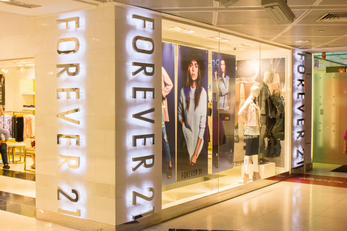 探索Forever 21最新潮流 壁紙 — 購物中心內明亮照明的Forever 21店舖正面，配有發光標誌和展示時尚服裝的人體模型。