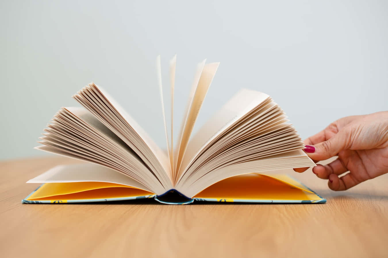 手在木桌上翻動打開的書的書頁。