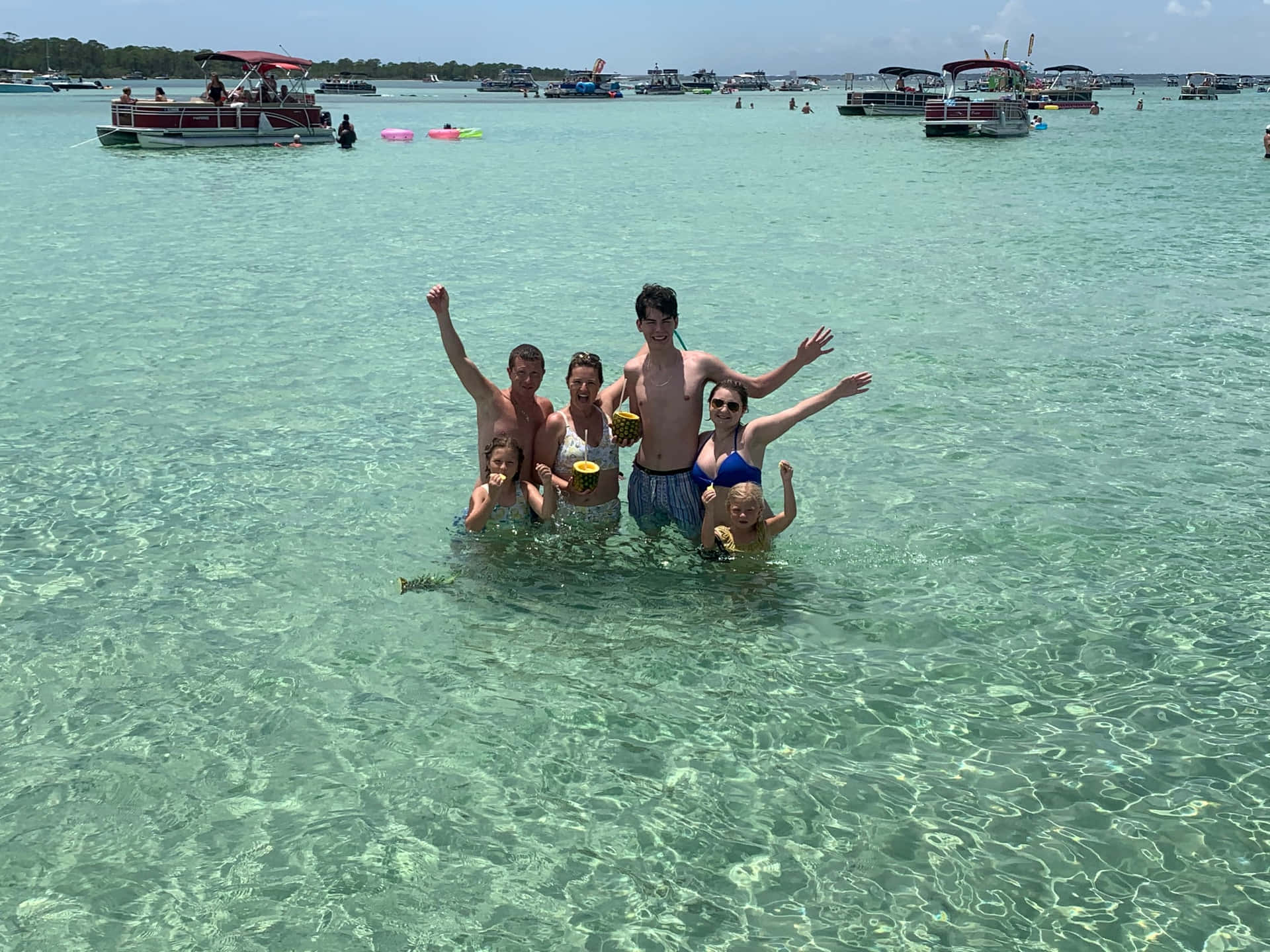 家人在清澈的碧綠海水中享受，背景有船隻