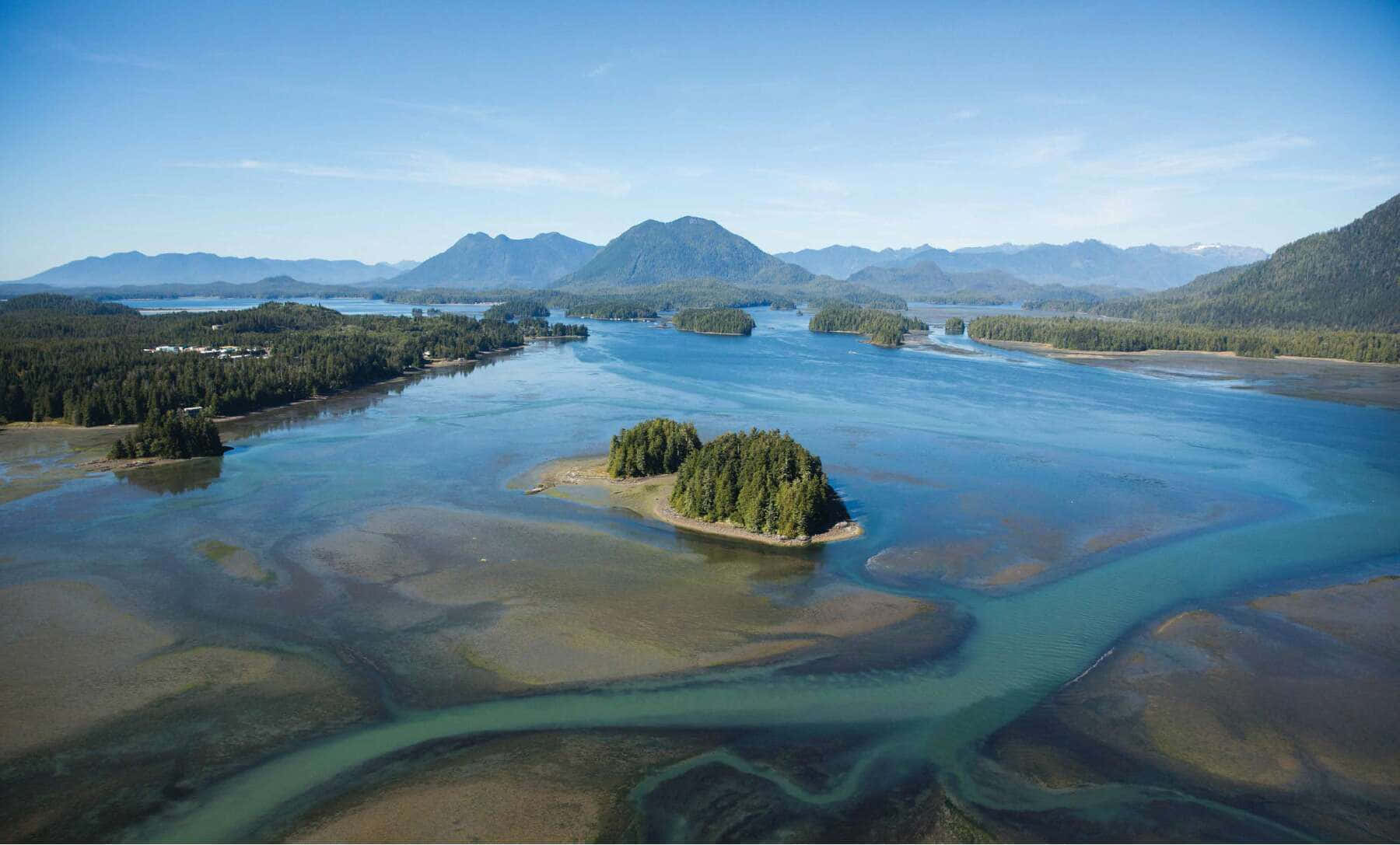 探索地球的生物圈 壁紙 — 鳥瞰圖：蜿蜒的河流在蔚藍天空下分成碧綠水道，環繞著森林覆蓋的島嶼和遠山。