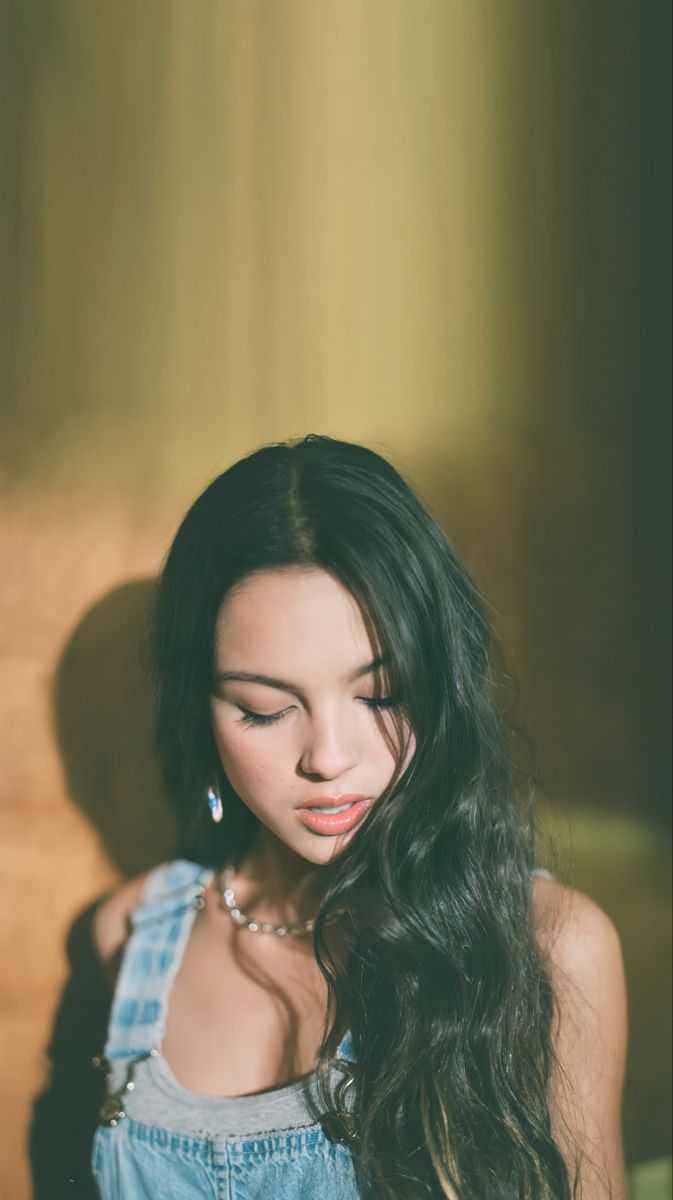 穿著牛仔工人褲的長黑髮年輕女性在柔和的金色燈光中低頭。