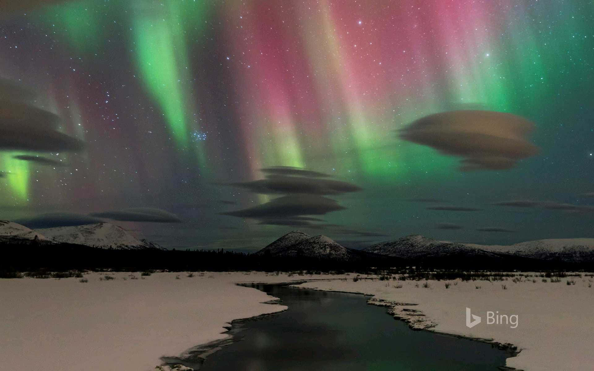 極光在夜間照耀著白雪覆蓋的山脈和冰凍的河流。