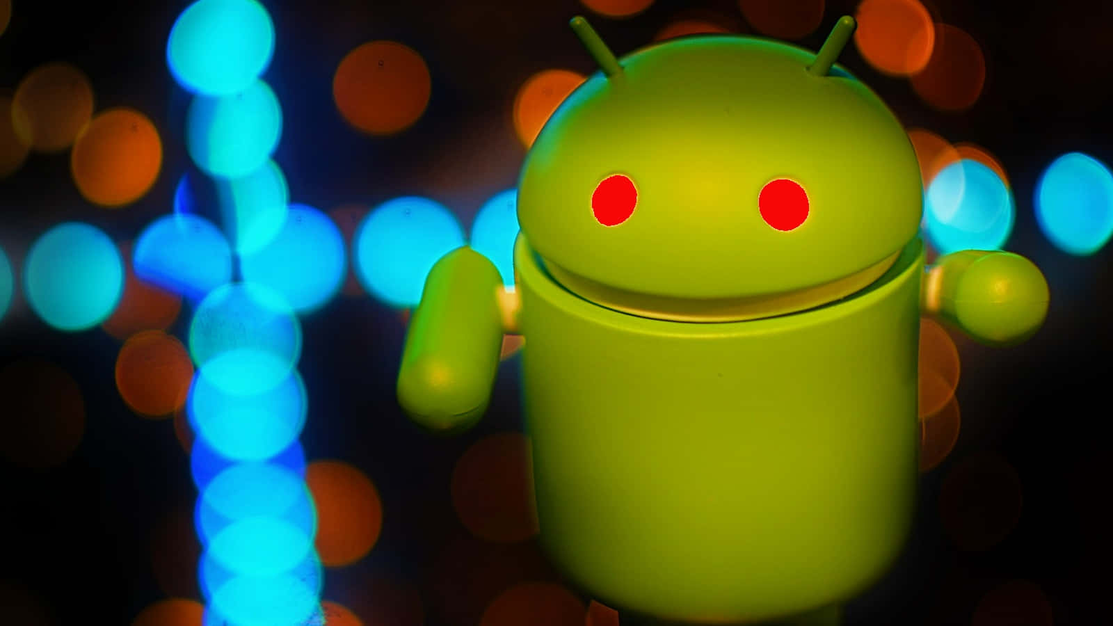 探索安卓世界 壁紙 — 一個發光的綠色Android機械人公仔，在藍色和橙色燈光的鮮豔散景背景前站立。