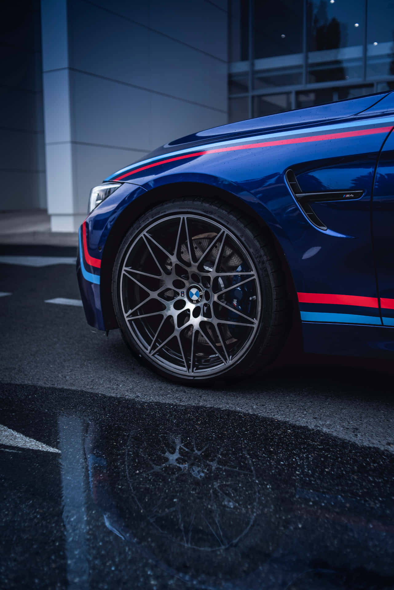 帶有賽車條紋的藍色BMW M4夜間停在濕漉漉的路面上。