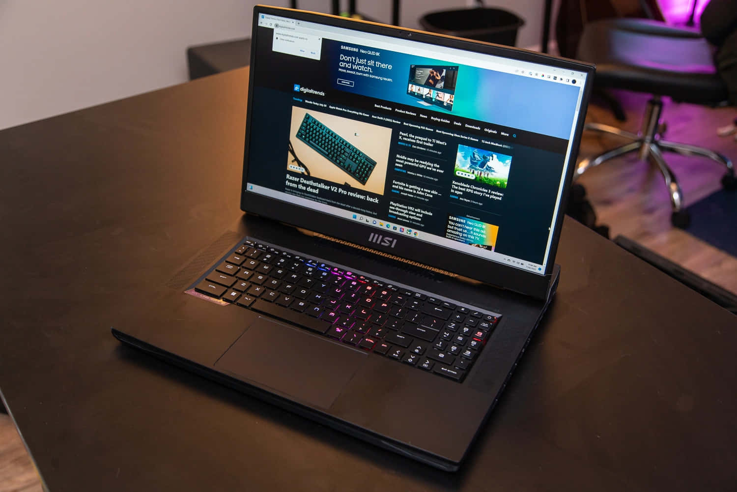 黑色 MSI 遊戲筆記型電腦配備 RGB 鍵盤，放在木桌上顯示科技網站。