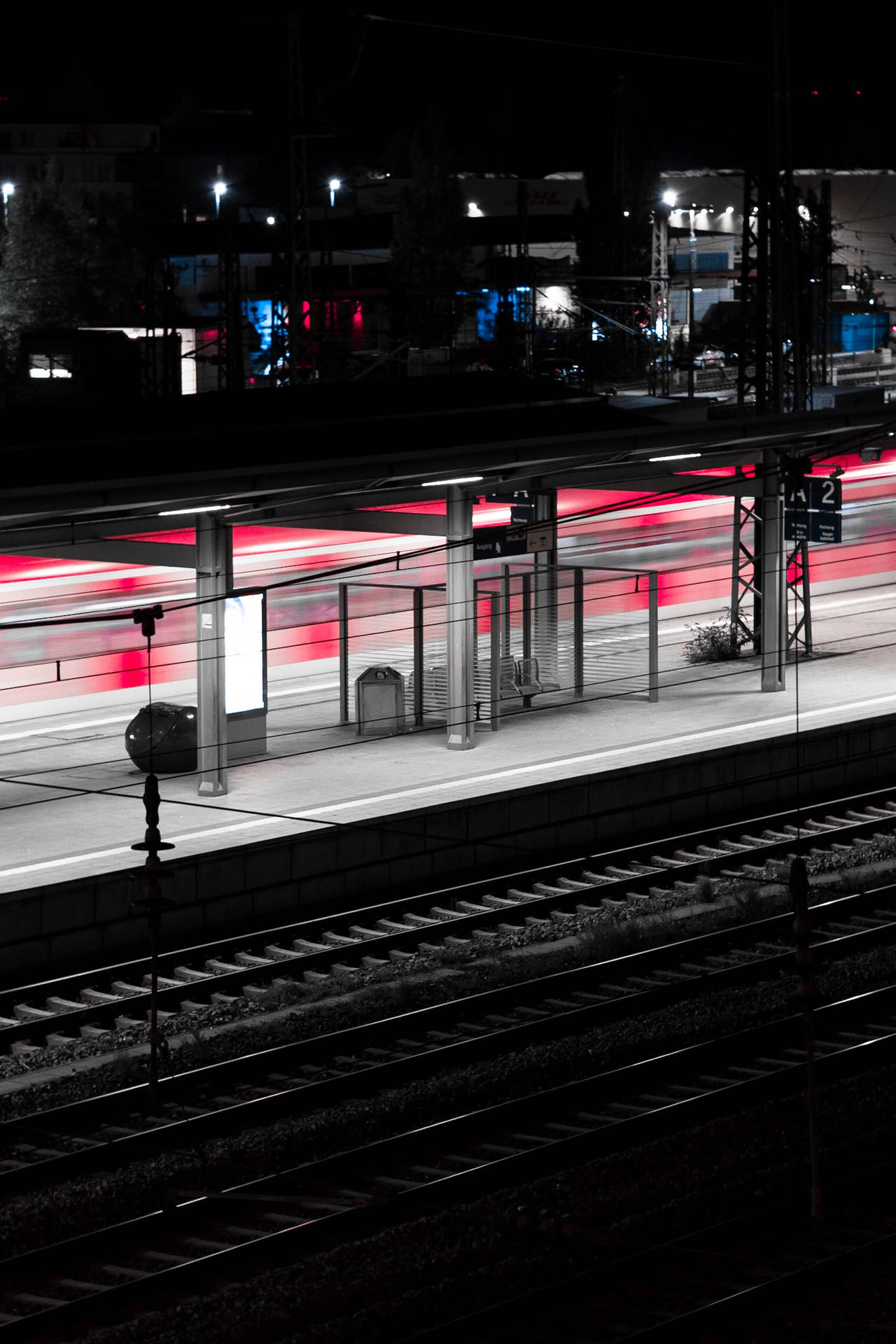 夜間火車站，黑暗鐵軌上有移動火車的紅色光跡。