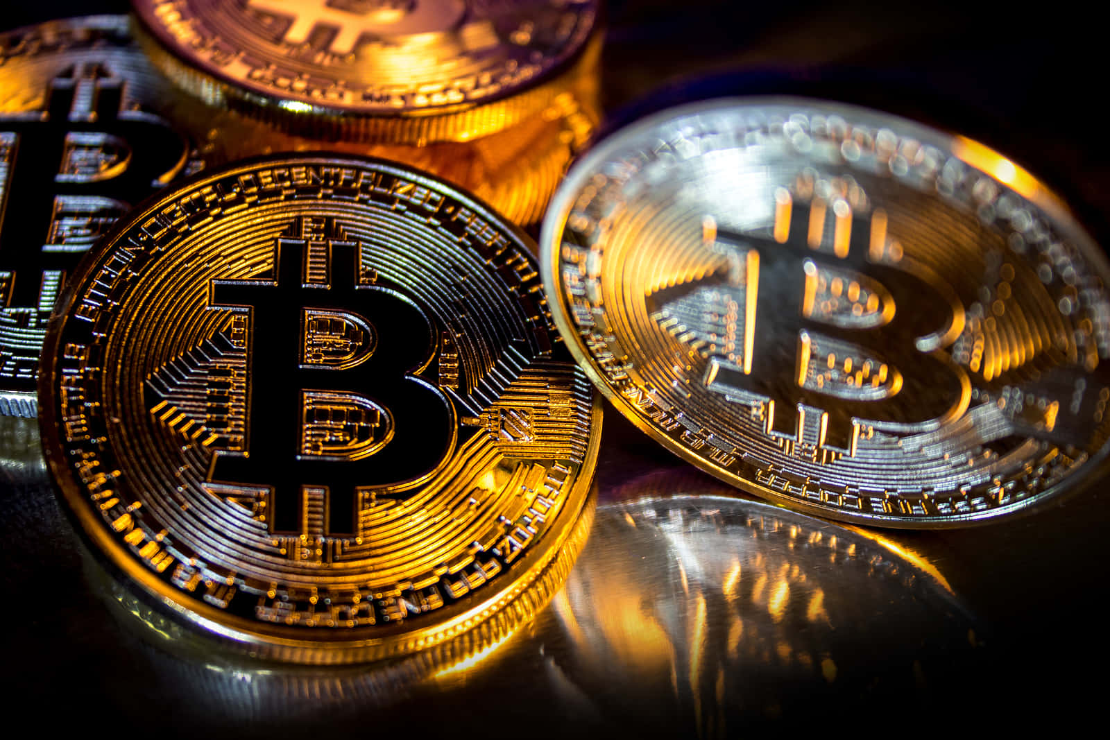探索比特幣的優勢 壁紙 — 閃亮的金色和銀色比特幣硬幣在黑暗表面上反射溫暖光線，景深較淺。