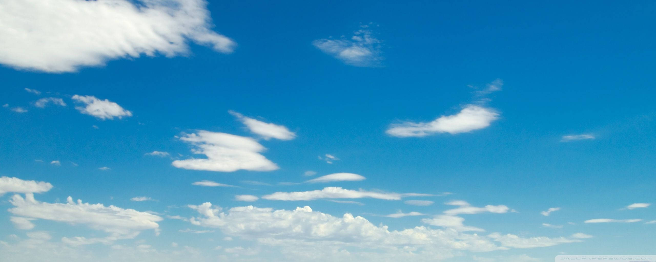 探索沙漠天空的藍色調 壁紙 — 廣闊明亮的藍天，佈滿散落的蓬鬆白雲，在清晰日光下。