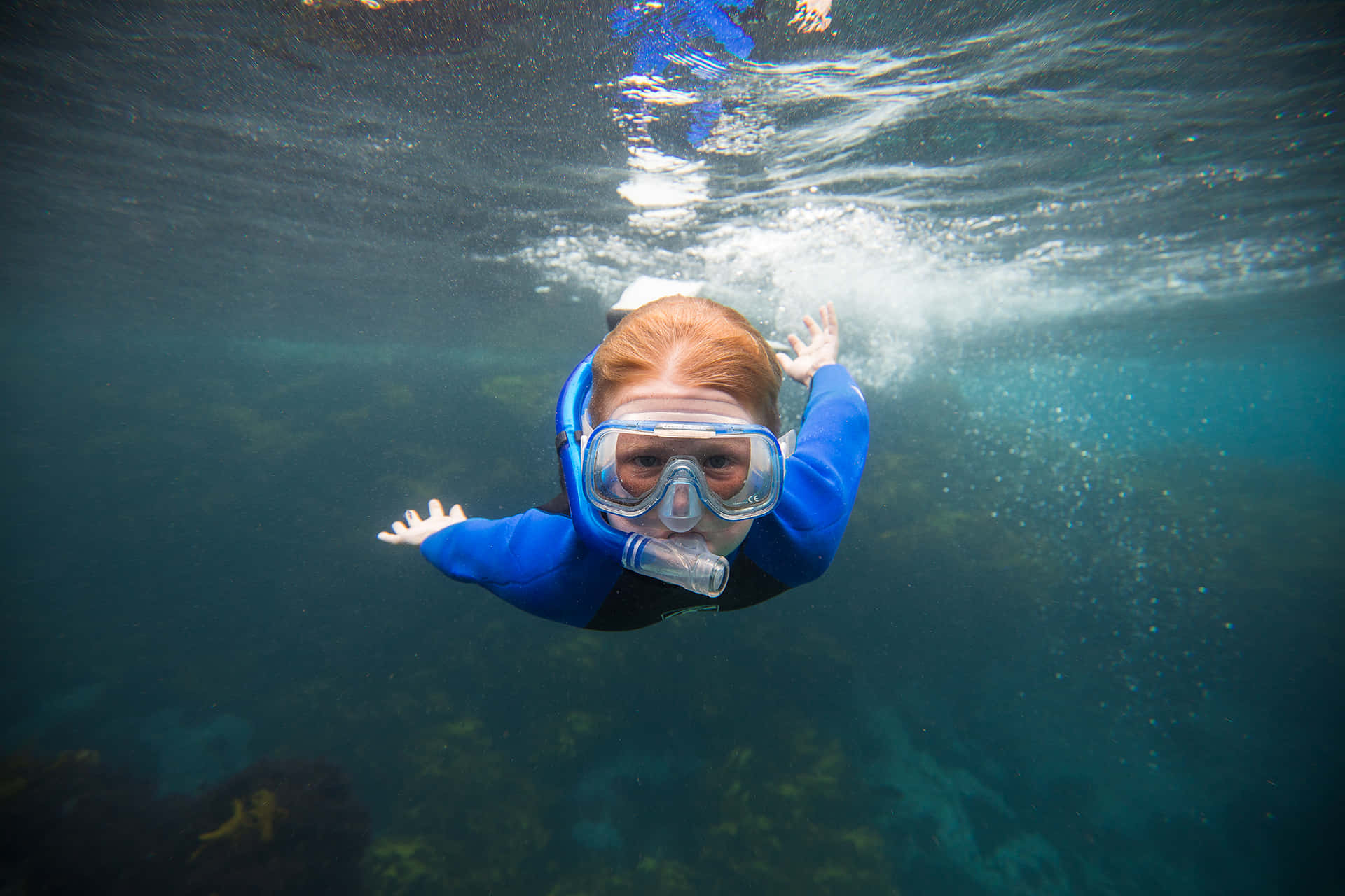 探索海洋與其生物的奇觀 壁紙 — 一位穿著藍色潛水衣和浮潛裝備的年輕女孩在水下游泳，雙臂伸向陽光照耀的水面。