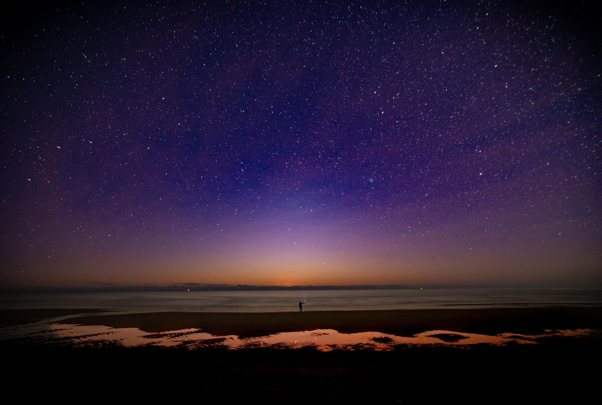 一個人在星空下站在海灘上的剪影，天空呈紫色和橙色。