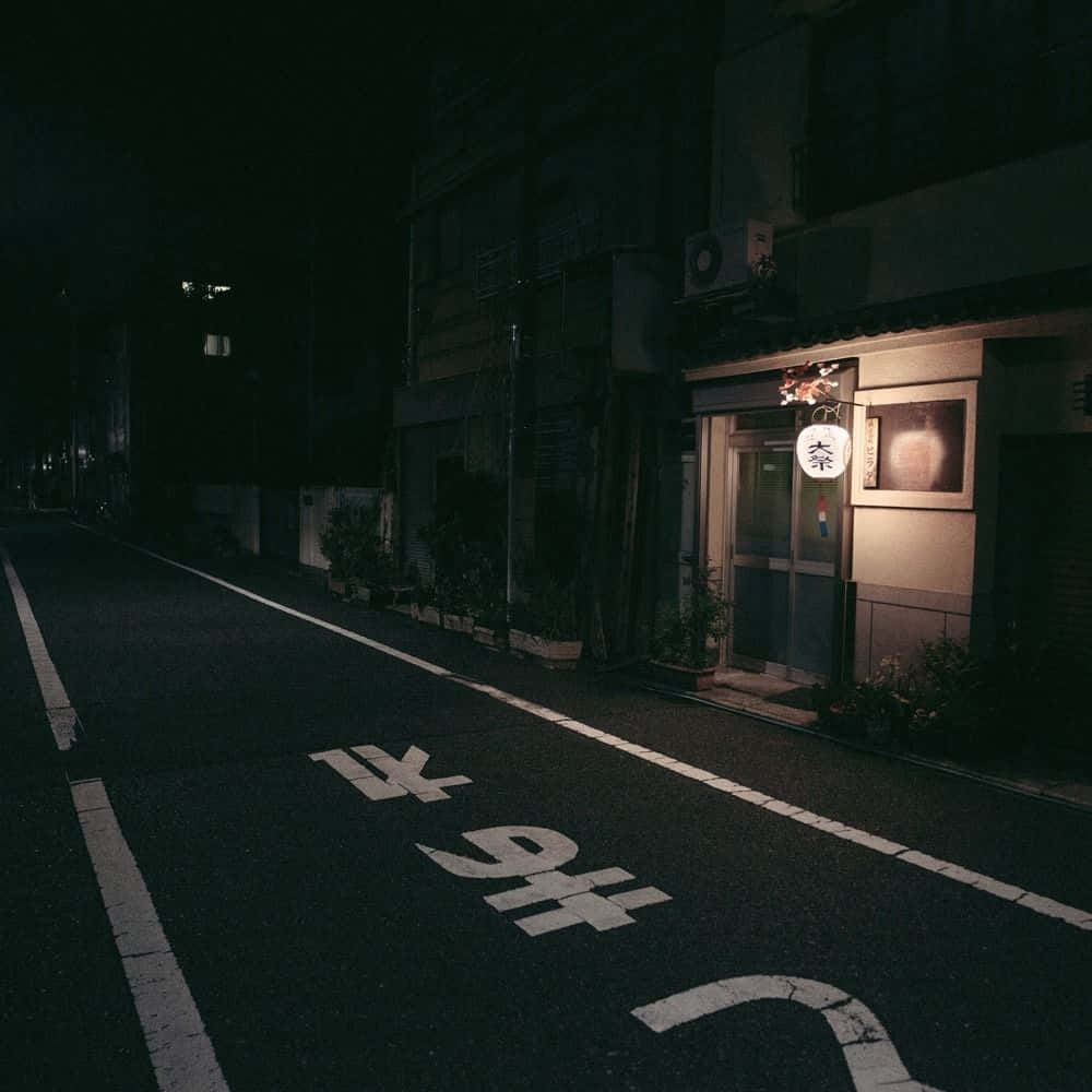 探索灰色的無限可能 壁紙 — 一條寧靜的日本街道在夜晚被小商店外一盞發光的燈籠照亮。