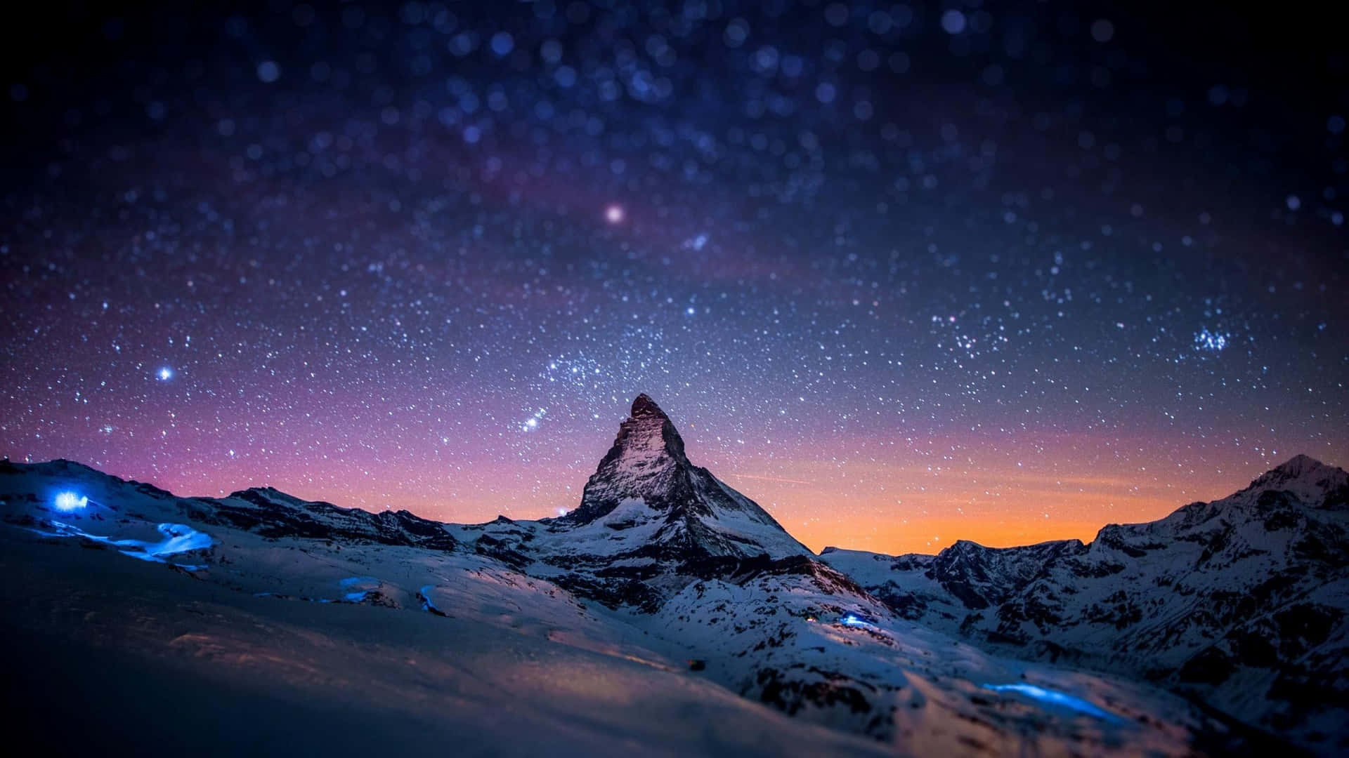 星空暮色下白雪覆蓋的山峰，下方有發光的藍色燈光。