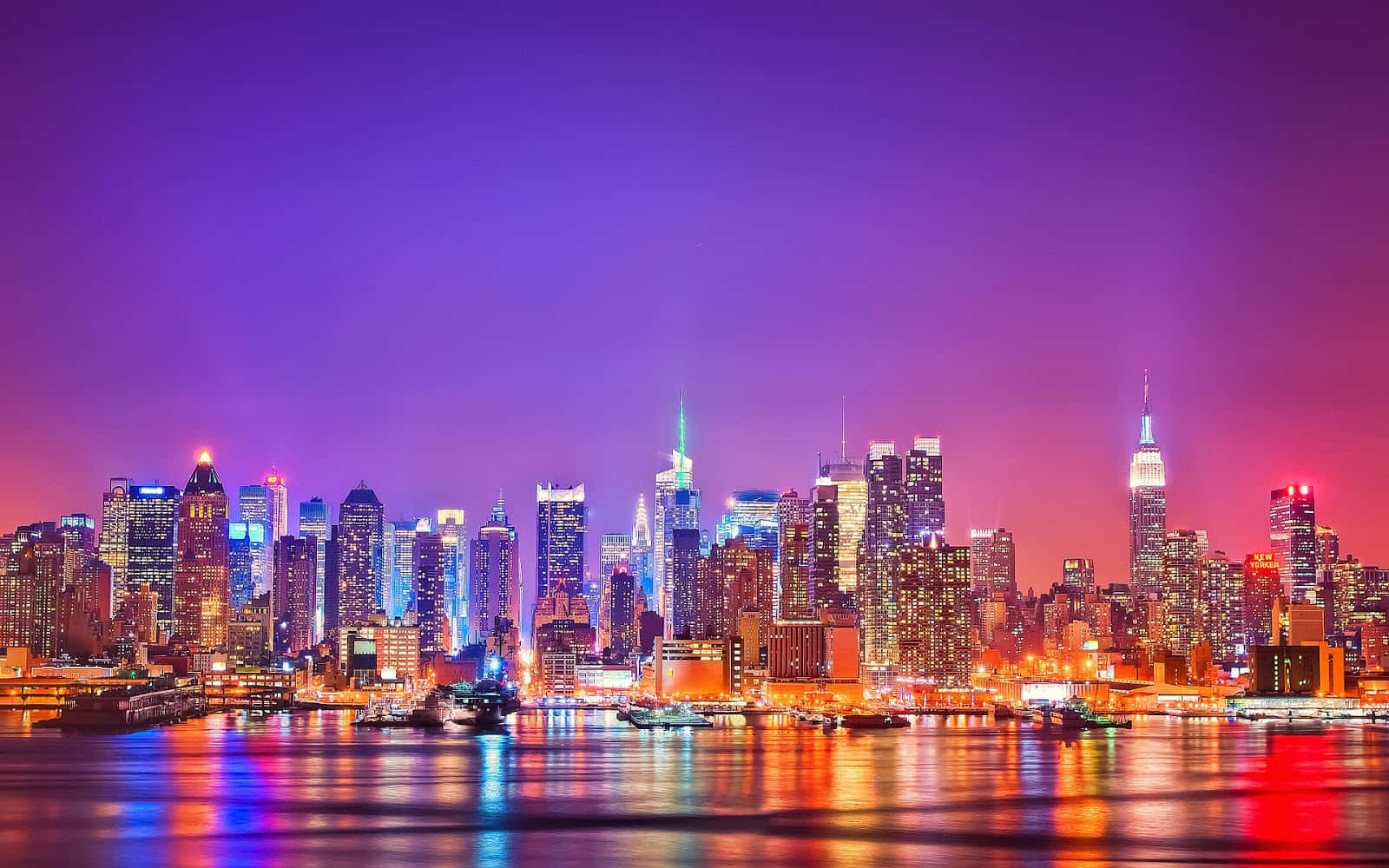 探索紐約市的活力能量 壁紙 — 紐約充滿活力的夜景，閃爍的摩天大樓在紫色和粉紅色的天空下倒映在水中。
