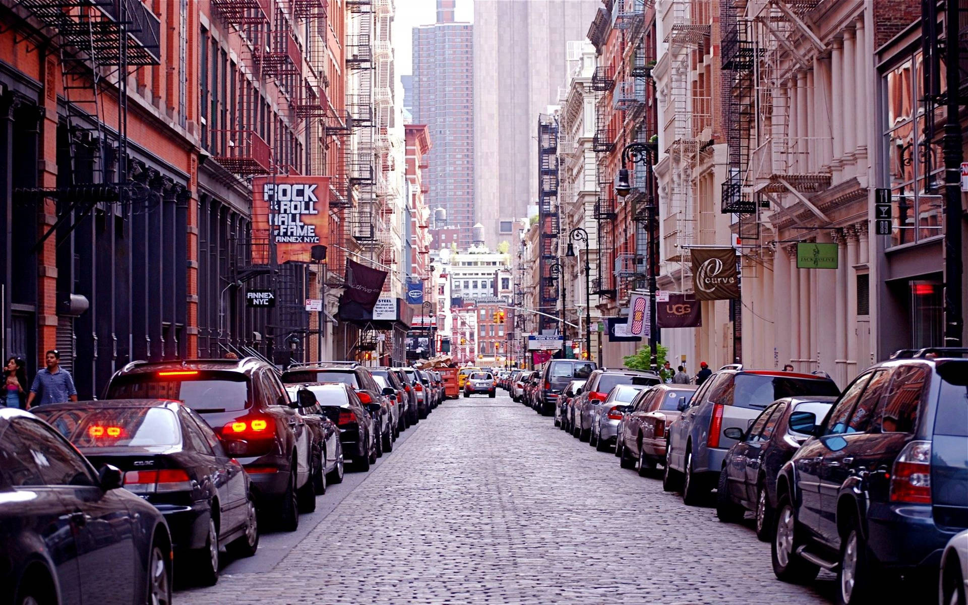 城市街道，停有汽車和磚砌建築，天空朦朧。
