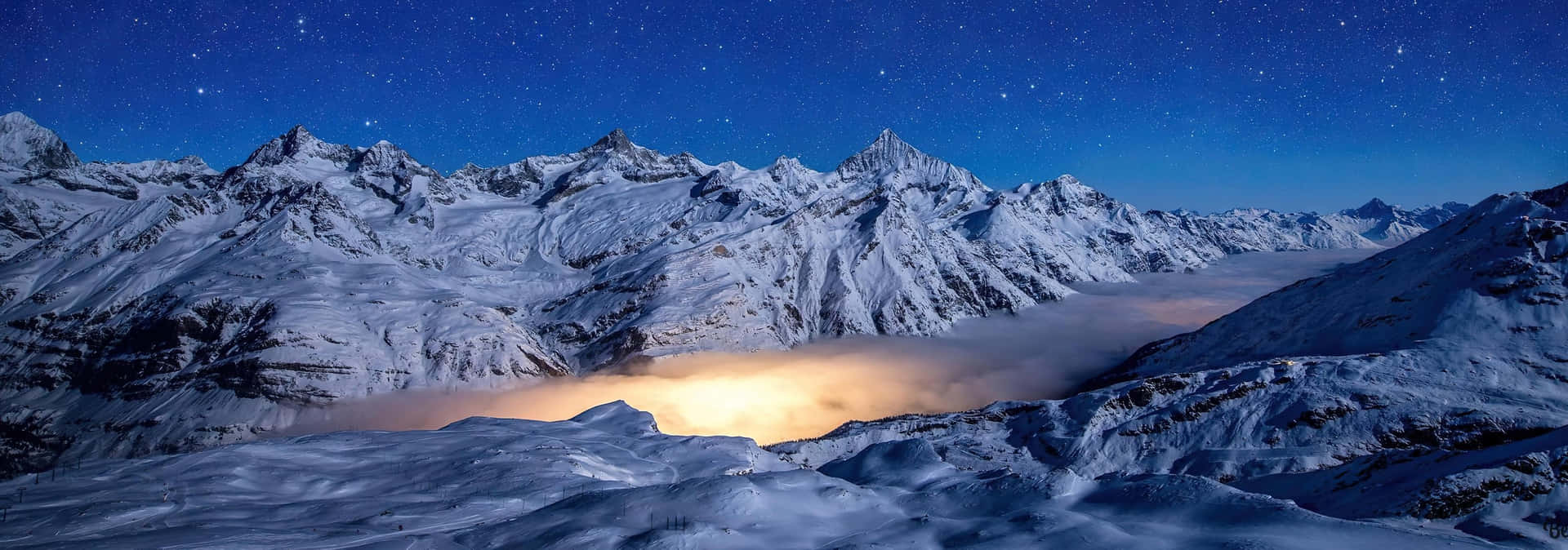 星空下積雪的山脈，下方有發光的雲層