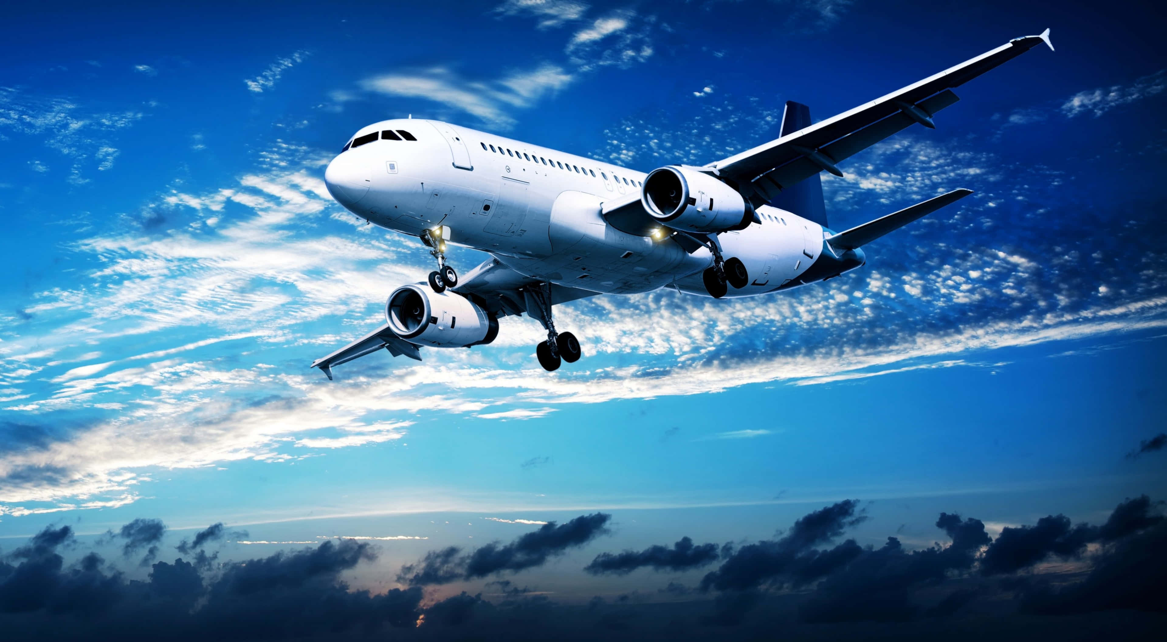 探索迪士尼《飛機》的開放天空 4K解析度 壁紙 — 一架白色客機在暮色中翱翔於蔚藍天空，天空點綴著縷縷薄雲。