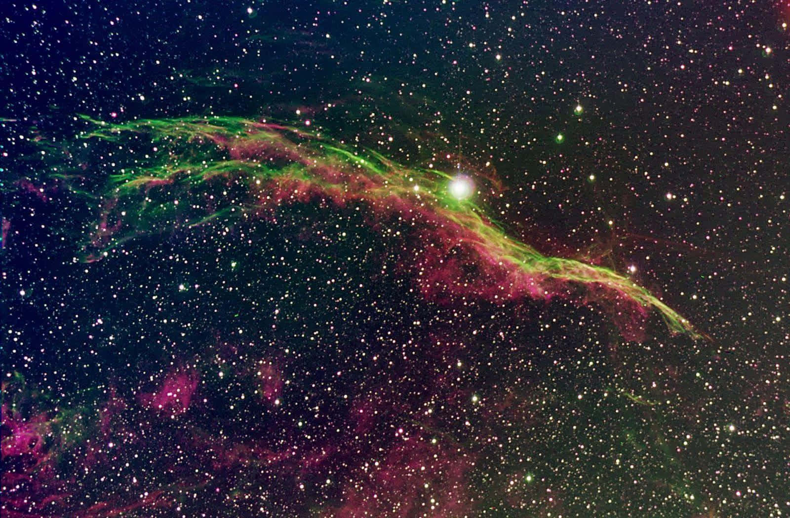 在深空中無數恆星之間發光的充滿活力的綠色和粉紅色星雲。